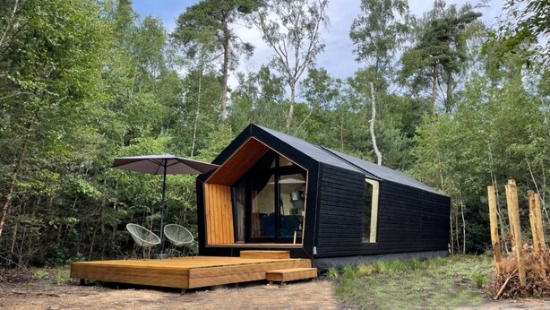 Una moderna cabina con una terrazza in legno, ampie finestre e una zona pranzo con sedie.