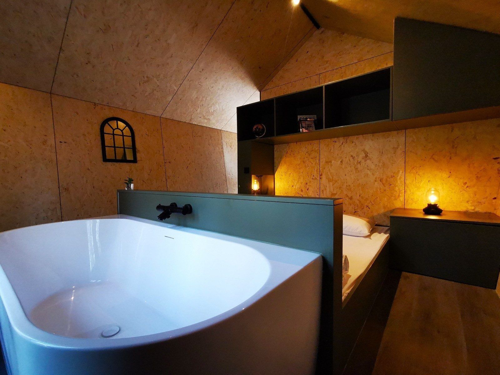 A room with a large bathtub, a small window, and a shelf with items.
