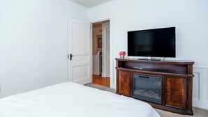 A bedroom with a bed, a television on a wooden cabinet, and a door leading to another room. - Parkins Mill Bungalow (Greenville)