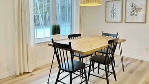 Un comedor con mesa de madera y sillas negras, lámpara colgante y cuadros en la pared.