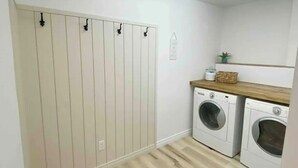 Un lavadero con suelo de madera, dos lavadoras, un mostrador de madera y un tendedero fijado a la pared.