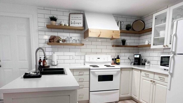 Una cocina moderna con armarios blancos, horno doble, un lavabo y estantes de madera.