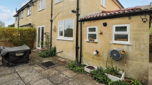 A two-story house with a tiled roof, a satellite dish, and a garden with potted plants and a barbecue grill. - Highbury (Bath)