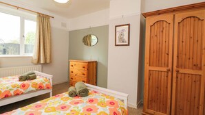 A bedroom with two beds, a wooden wardrobe, a dresser, a window with curtains, and a wall-mounted mirror. - Highbury (Bath)