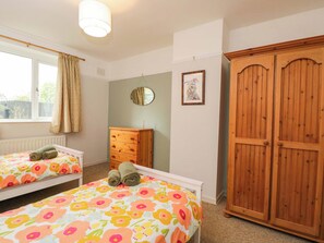 A bedroom with two beds, a wooden wardrobe, a dresser, a window with curtains, and a wall-mounted mirror. - Highbury (Bath)