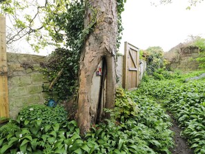 A tree with a wooden door, a stone wall, and a garden with various plants. - Highbury (Bath)