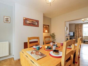 Uma sala de jantar com uma mesa de madeira, cadeiras, um quadro e um vaso com planta.