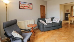 A living room with a grey sofa, a grey armchair, a wooden floor, a radiator, a painting on the wall, and a dining area in the background. - Highbury (Bath)