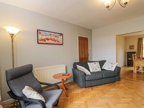 A living room with a grey sofa, a grey armchair, a wooden floor, a radiator, a painting on the wall, and a dining area in the background. - Highbury (Bath)