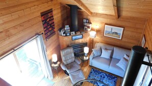 A wooden cabin interior with a sofa, chairs, a fireplace, and a framed picture on the wall. - Iconic 70s style cute condo cottage in Deck 2, on a pond! (CS0055) (Wellfleet)