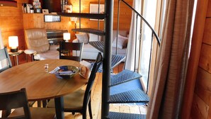 A wooden interior with a dining table, chairs, a sofa, a staircase, and a window. - Iconic 70s style cute condo cottage in Deck 2, on a pond! (CS0055) (Wellfleet)
