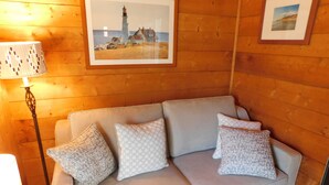 A wooden interior with a sofa, patterned cushions, a framed picture of a lighthouse, and a floor lamp. - Iconic 70s style cute condo cottage in Deck 2, on a pond! (CS0055) (Wellfleet)