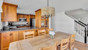 Een keuken met houten kastjes, een roestvrijstalen koelkast, een magnetron en een eettafel met stoelen.
