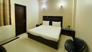 Une chambre à coucher comprenant un lit, une chaise, une table de chevet, une lampe fixée au mur, un ventilateur de plafond et une porte.