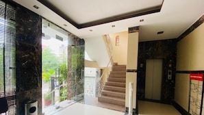 Un hall d’entrée avec une colonne en marbre, un escalier et une porte vitrée donnant sur l’extérieur.