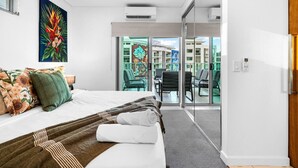 Et moderne hotelværelse med en seng, et maleri, en balkon med stole og udsigt til bygninger.