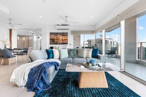 A modern living room with a sofa, coffee table, and a large window offering a view of the city. - Zen Crystal Tide Balcony - Pool - Gym - Seaview (Darwin)