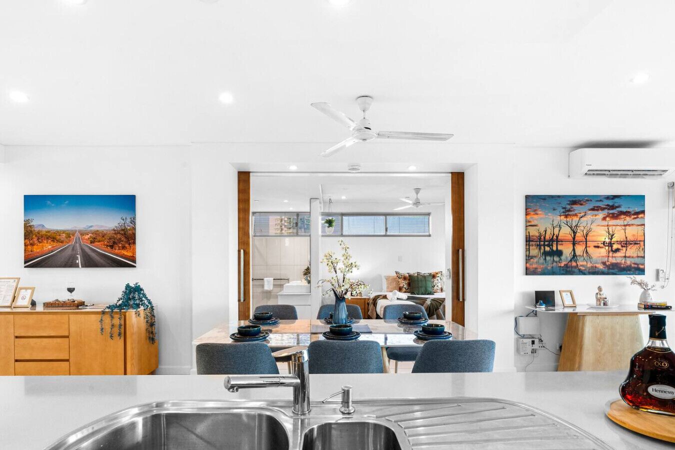 A modern kitchen with a central island, a dining area with blue chairs, and a view into a bedroom.