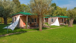 A wooden cabin with a green roof, a porch, and a white tent-like structure. - Ferienhaus mit Kamin am Achterwasser in Lutow (Luetow)