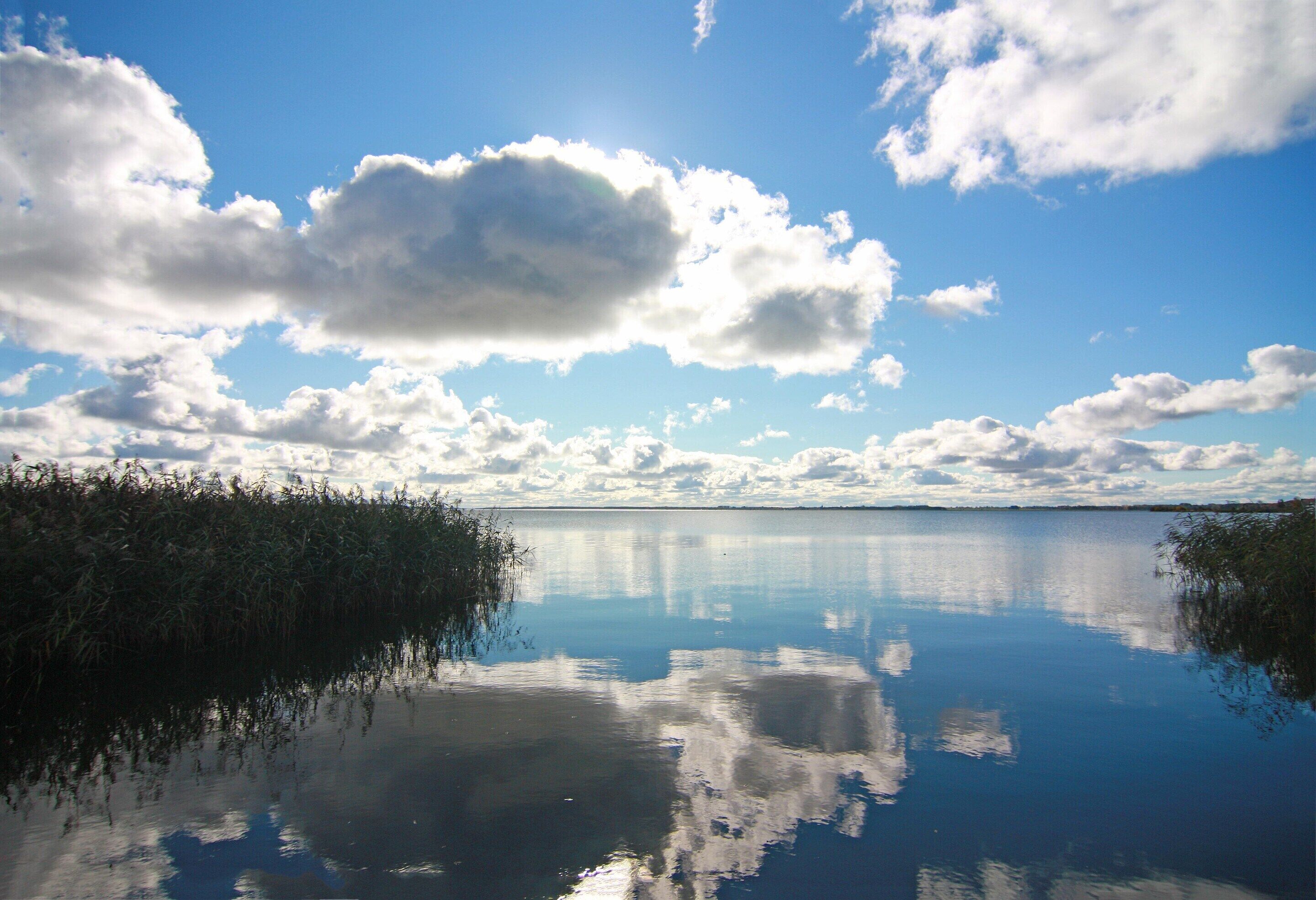 A calm lake with reflections of clouds and a clear sky.