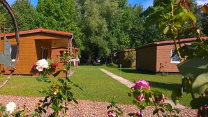 A row of wooden cabins with a grassy lawn and trees in the background. - Ferienhaus mit Kamin am Achterwasser in Lutow (Luetow)