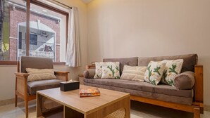 Ein Wohnzimmer mit einer Couch, zwei Sesseln, einem Couchtisch und einem Fenster mit Blick auf ein Gebäude.
