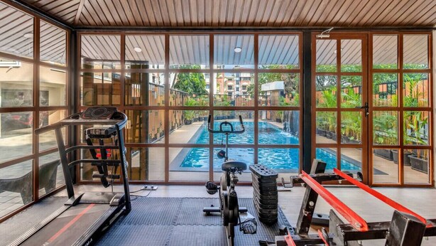 Ein Fitnessraum mit Trainingsgeräten, Laufband und Blick auf ein Außen-Schwimmbecken durch große Fenster.
