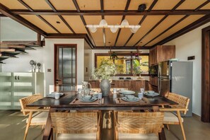 A modern kitchen with a dining area, featuring a wooden table, chairs, and a hanging light fixture. - Casa Melina - 1 5BR Private Beach House in Anjuna (Anjuna)