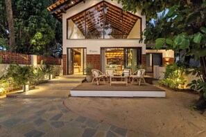 A modern two-story house with a patio area featuring wicker furniture and potted plants. - Casa Melina - 1 5BR Private Beach House in Anjuna (Anjuna)