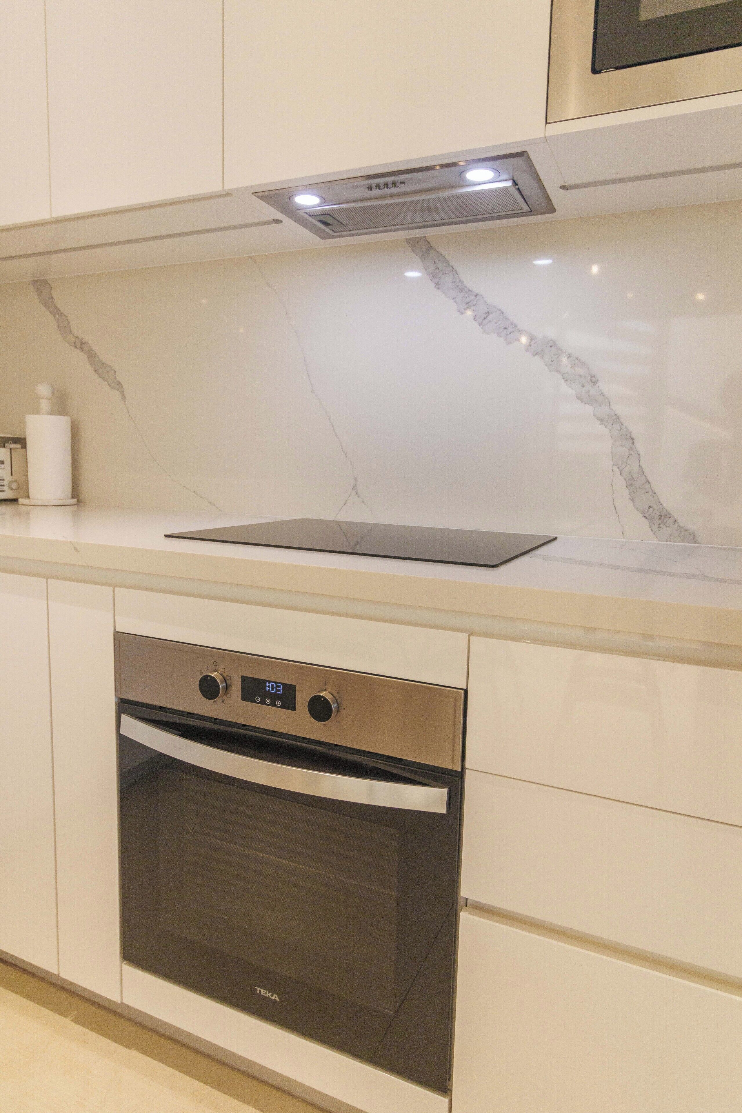 A modern kitchen with a built-in oven, a digital clock, and a marble backsplash.