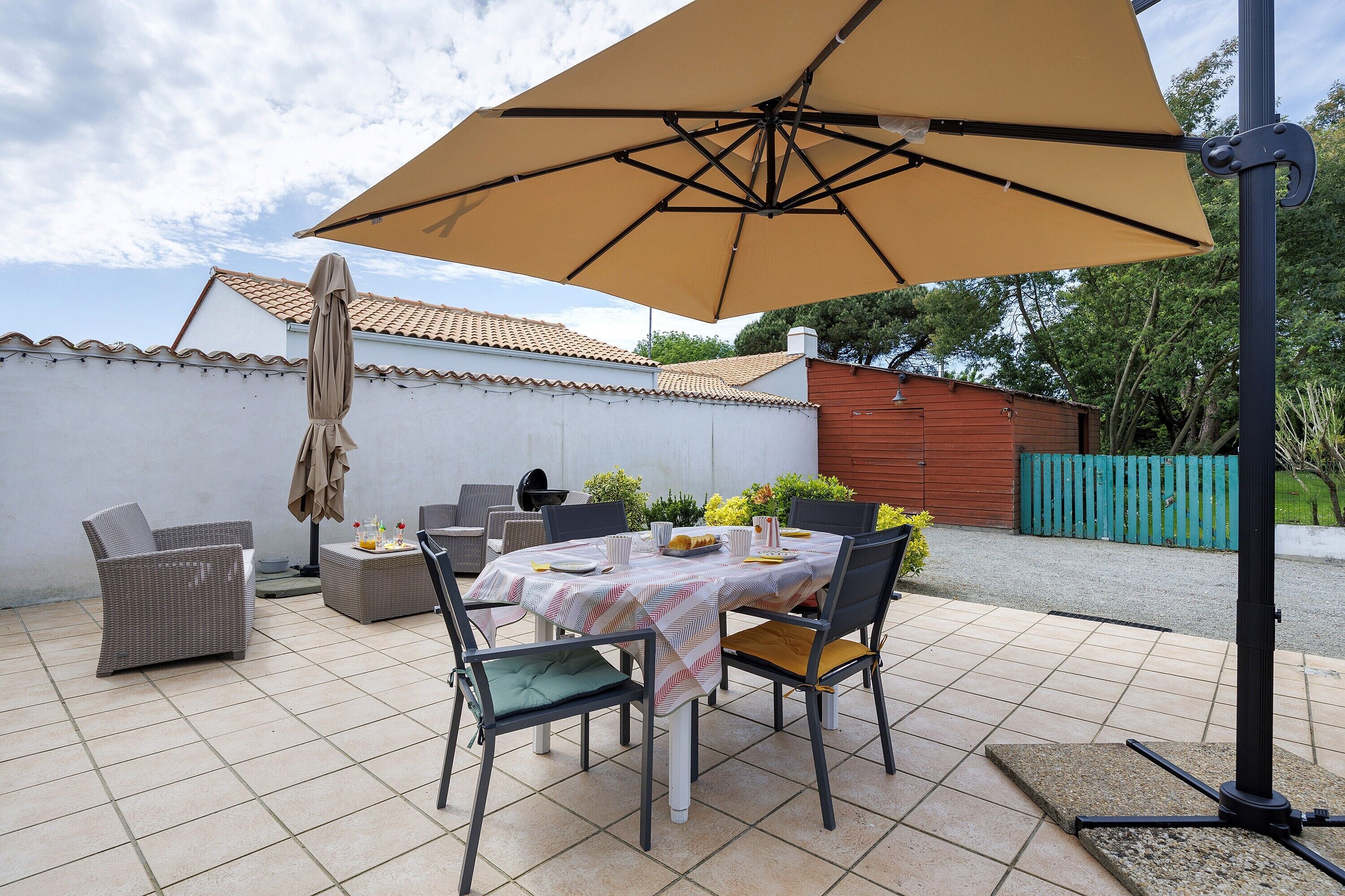 A patio with a table and chairs, a large umbrella, and a wicker chair.