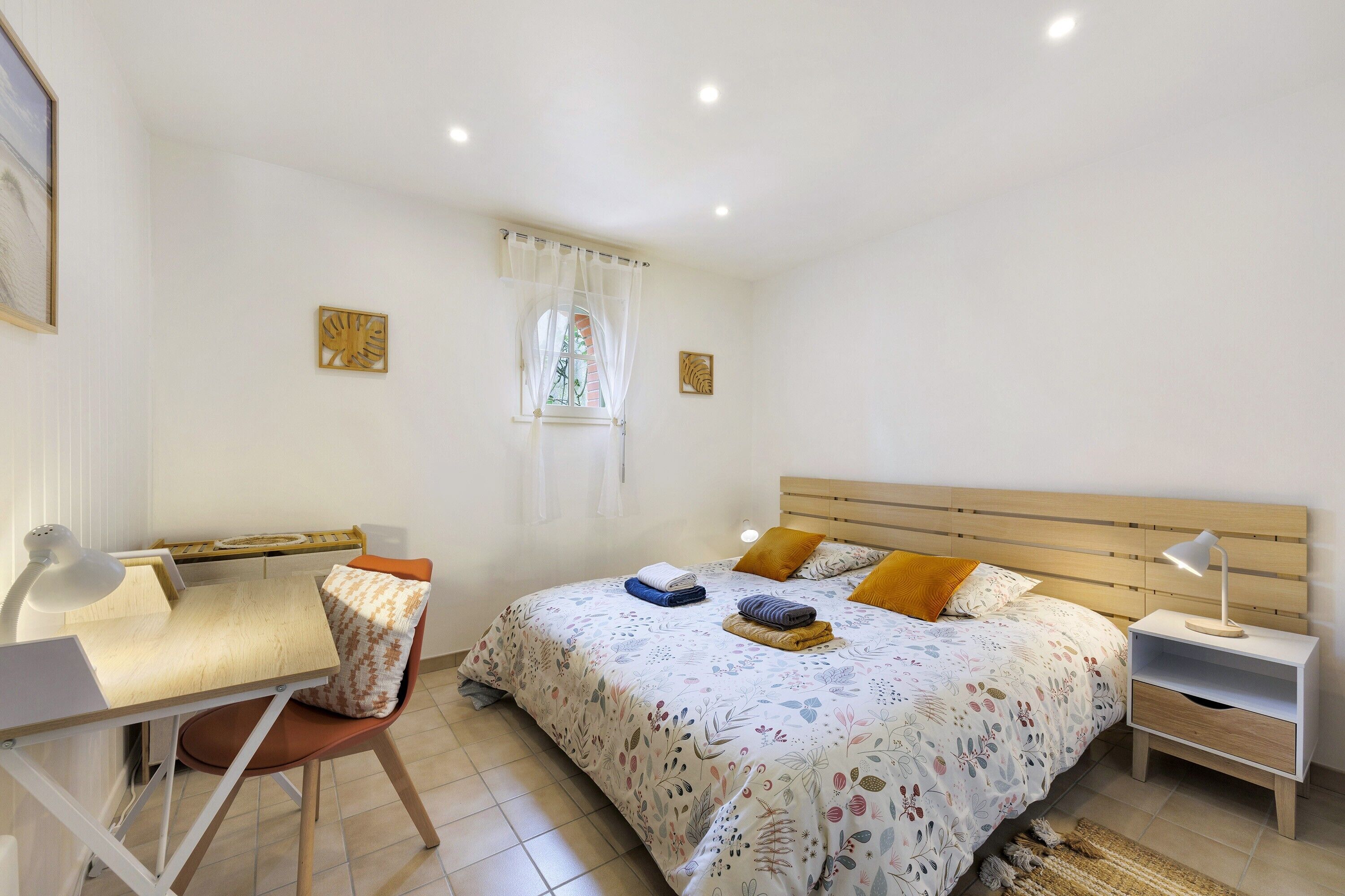 Une chambre à coucher comprenant un lit, une table de chevet, un bureau, une chaise et une fenêtre avec des rideaux.