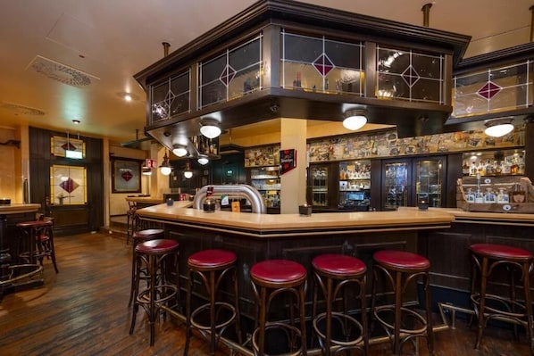 A bar area with a counter, stools, and a variety of bottles and glasses.