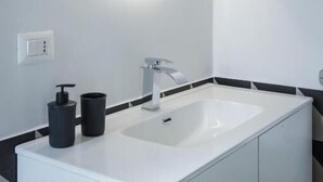 Un baño moderno con un lavamanos rectangular, un espejo redondo con luz y azulejos blancos y negros.