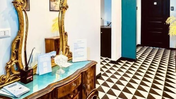 Un pasillo con suelo de cuadros, un aparador de madera con espejo y una puerta con un letrero de neón.