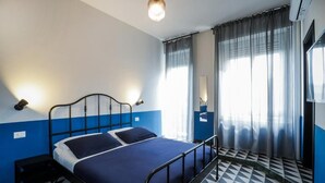 A room with a bed, a nightstand, a lamp, a window with curtains, and a patterned floor. - Nuccia Urban Loft (Naples)