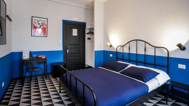 A room with a bed, a desk, a chair, a door, and a poster on the wall. - Nuccia Urban Loft (Naples)