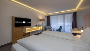 A hotel room with a bed, a desk with a lamp, a chair, a TV, and a window with curtains. - Relaxing Unit Pets Allowed Indoor Swimming Pool With Forest Trails (Arnsberg)