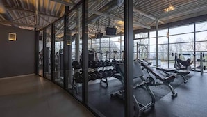 Una palestra con attrezzature per esercizi, ampie finestre e un moderno soffitto industriale.