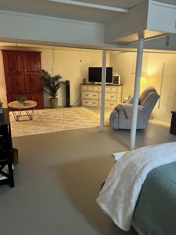 A room with a bed, a chair, a small table, a television, and a cabinet.