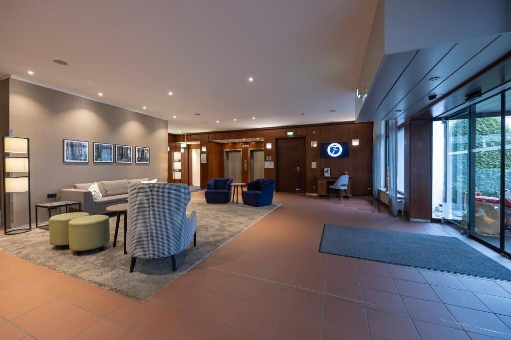 Eine moderne Lobby mit einer Couch, Sesseln, einem Couchtisch und einer Rezeption.