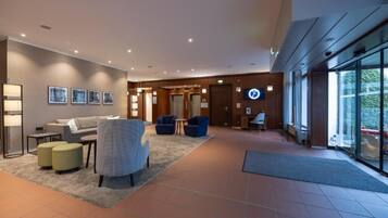 Eine moderne Lobby mit einer Couch, Sesseln, einem Couchtisch und einer Rezeption.