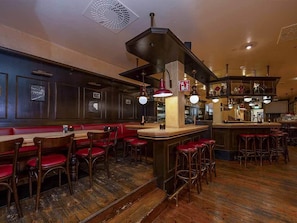 A bar area with wooden bar stools, a counter, and a seating area with red upholstered chairs.