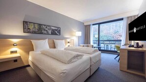 Ein Hotelzimmer mit zwei Betten, einem Schreibtisch, einem Sessel, einem Fernseher und einem Balkon mit Blick.