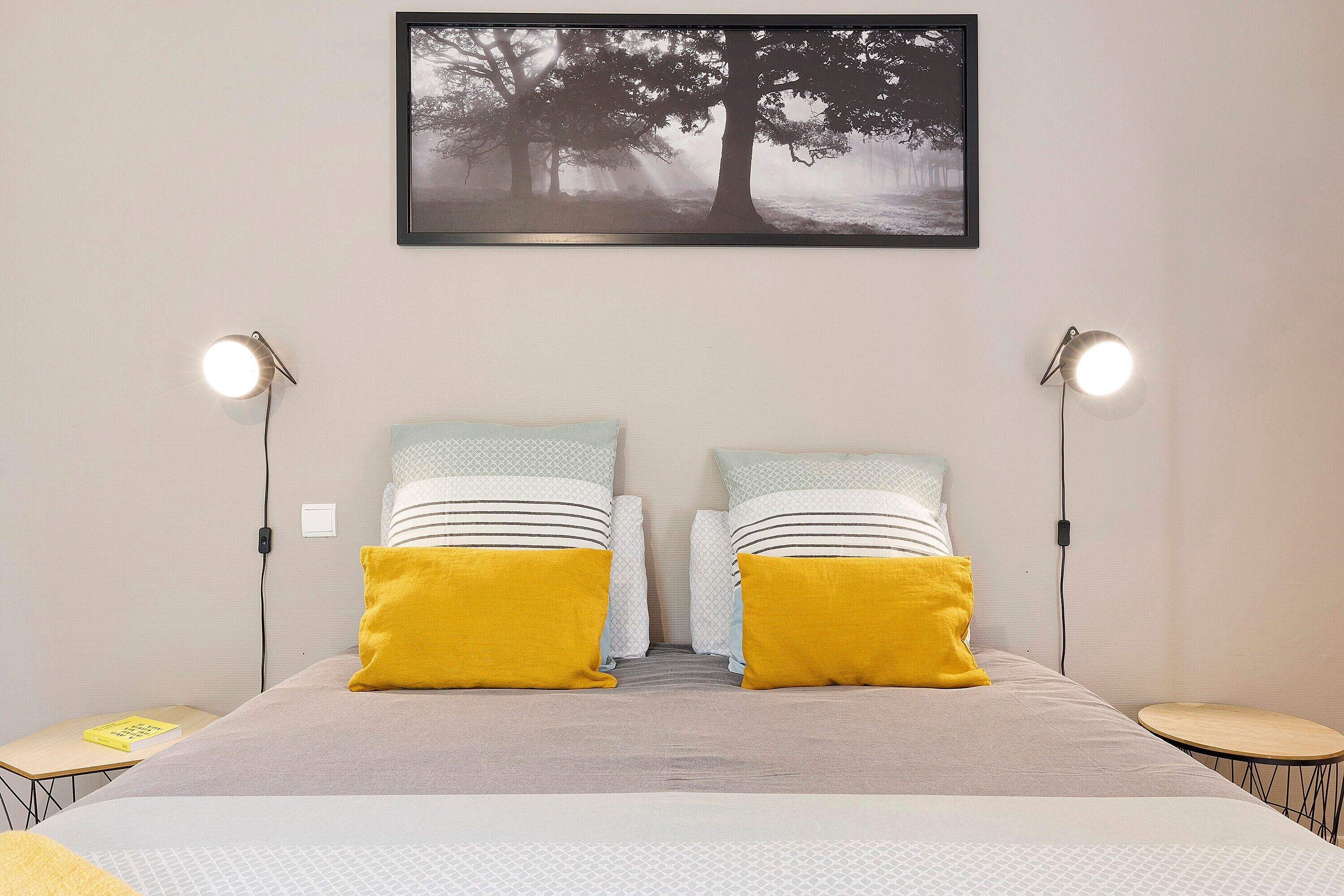 Een slaapkamer met een bed, twee bedlampen, een nachtkastje en een ingelijst schilderij aan de muur.