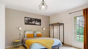 A bedroom with a bed, bedside lamps, a picture on the wall, a window with curtains, and a hanging rack. - Gîte La Rémondière – 20 min from Puy du Fou (Pouzauges)
