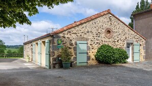 A stone building with a tiled roof, a sign indicating a location, and a small green bush. - Gîte La Rémondière – 20 min from Puy du Fou (Pouzauges)