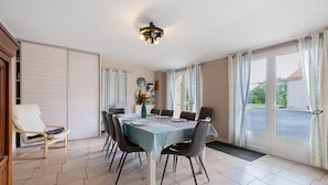 A dining area with a table set for four, chairs, a ceiling light fixture, and a view through a glass door. - Gîte La Rémondière – 20 min from Puy du Fou (Pouzauges)
