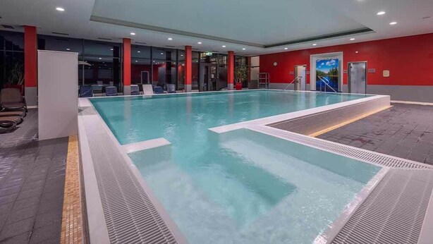 Ein Hallenbad mit klarem Wasser, umgeben von roten Wänden und Glastüren.