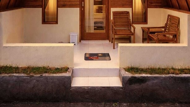 A wooden cabin with a pitched roof, a front door, a small porch with two chairs, and a single light fixture above the door. - Sunflower Villa (Gili Trawangan)